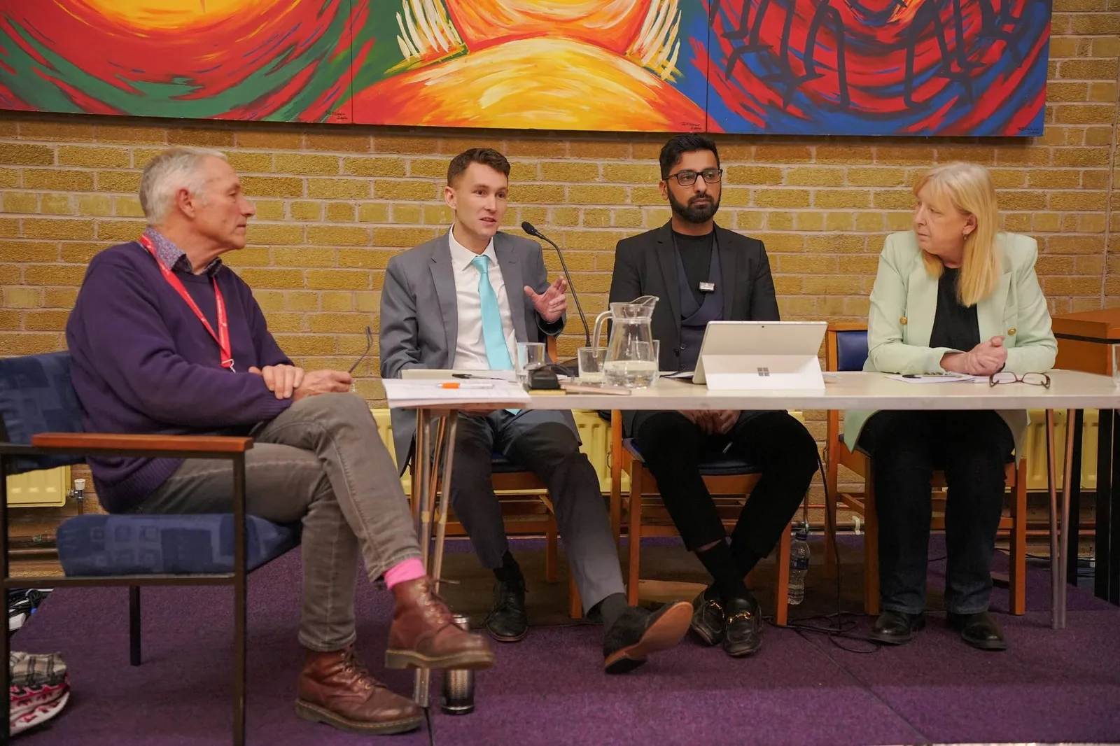 Four participants seated at the front of Wesley Hall, with a panellist speaking into a microphone.